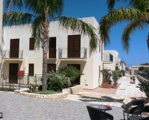 a white building with palm trees in front of it at Hotel Sikania in San Vito lo Capo