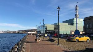 a street with cars and people and dogs on a sidewalk next to the water at Ann St Vacation Apartment Greenock United Kingdom in Greenock