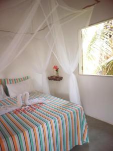 1 dormitorio con 1 cama con manta a rayas y ventana en Flor da Ilha Flats en Ilha de Boipeba