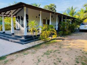 a white house with a porch and palm trees at Garden Oasis with 1 Bedroom & 1 Bathroom in Batticaloa