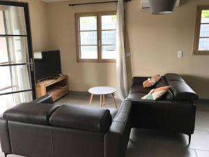 ein Wohnzimmer mit einer schwarzen Ledercouch und einem Tisch in der Unterkunft Villa l'Amoureuse 3 in Saint-Paul-le-Jeune