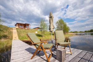 zwei Stühle und ein Regenschirm auf einem Dock neben einem See in der Unterkunft Pineplace twins NIDA in Žaugėdai