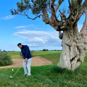 Un uomo sta giocando a golf vicino a un albero di Lamia Alchimia a Selva di Fasano