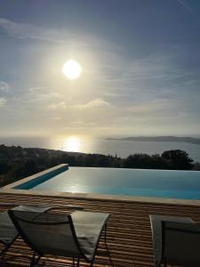 a swimming pool with two chairs and the sun in the sky at Appartement 4A villa cargese in Cargèse