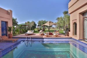 a swimming pool in a backyard with a patio with chairs and an umbrella at Villa May sur le Golf de la Palmeraie with Cooker and Butler included in Marrakech
