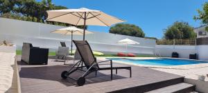 een stoel onder een parasol naast een zwembad bij Hospedaria do Almargem in Quarteira