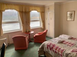 a bedroom with two chairs and a bed and two windows at Lochalsh Hotel with Views to the beautiful Isle of Skye in Kyle of Lochalsh