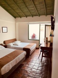 a bedroom with two beds and a desk and a window at Hotel Posada de San Agustin in Tunja