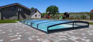 a glass pool with a playground in the background at Village Garden Family Guest House in Tiszakanyár