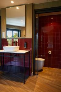 uma casa de banho com lavatório, WC e azulejos vermelhos em LATROUPE Prado Hostel em Madri