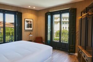 um quarto com uma cama branca e janelas grandes em LATROUPE Prado Hostel em Madri