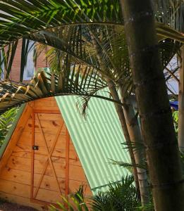 a wooden garage with a green door next to a palm tree at Hostel 4 Elementos - 200 metros da Praia de Pernambuco e do Mar Casado in Guarujá