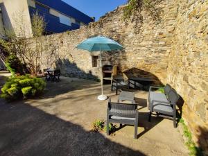 a patio with chairs and an umbrella next to a brick wall at Le TROPICA Appartement 2 chambres, plein Sud centre ville de VITRÉ in Vitré