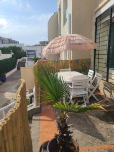um pátio com uma mesa, cadeiras e um guarda-sol em Les Portes de l'Océan avec piscine accessible l'été et sans plan sécheresse em El Harhoura