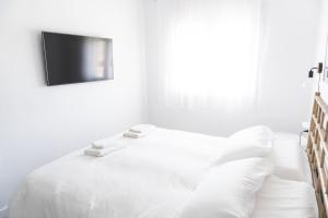 a white bedroom with a bed with a tv on the wall at Apartamento con Parking a 50m de la playa in Sant Antoni de Calonge