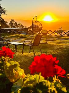 a sunset with chairs and a table and red flowers at Pousada Village Pôr do Sol in Campos do Jordão
