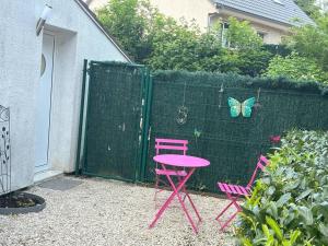 duas cadeiras cor-de-rosa e uma mesa rosa e uma borboleta numa cerca em Maison studio Le bois fleuri em Croissy-Beaubourg