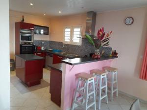 a kitchen with red cabinets and a counter with stools at Villa Sirius vue sur mer in Le Vauclin