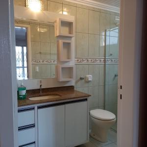 een badkamer met een toilet, een wastafel en een spiegel bij Espaço aconchegante em Criciúma in Criciúma