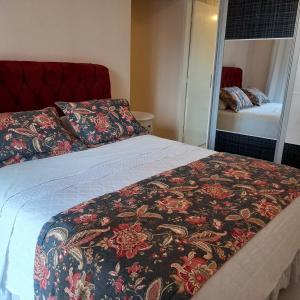 een slaapkamer met een bed met een bloemrijke deken en een spiegel bij Espaço aconchegante em Criciúma in Criciúma