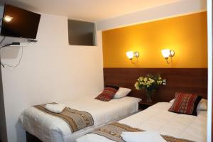 a room with two beds and a tv on the wall at Casa del Escultor in Cusco