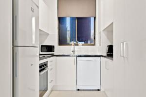 La cuisine blanche est équipée d'un évier et d'un réfrigérateur. dans l'établissement 2 bedrooms 2 baths with balcony and ocean views, across from ocean, à Alexandra Headland