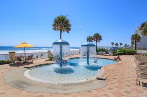 a pool with a palm tree in it next to the beach at Oceanfront Condo at Daytona Beach Resort in Daytona Beach