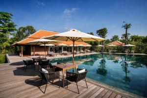 uma piscina com mesas, cadeiras e guarda-sóis em Farmhouse Resort & Spa em Kampong Chhnang