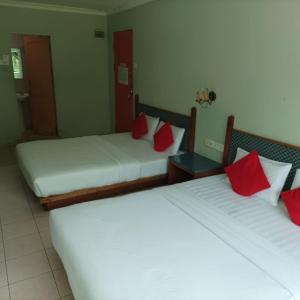 two beds in a hotel room with red pillows at Highway Inn in Mukah