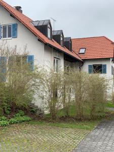a white house with a red roof and some bushes at Ferienwohnung 2 in Huglfing im Herzen vom 5 Seen Land Oberbayern in Huglfing