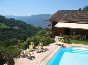 a swimming pool with chairs and a house and mountains at Chalet la Colombière in Sainte-Agnès