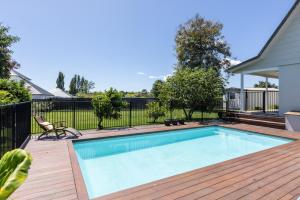 a swimming pool on a wooden deck with a fence at Live Large in the Village in Havelock North