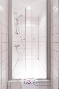 a shower with a glass door in a white tiled bathroom at Taste Hotel Jettingen in Jettingen-Scheppach