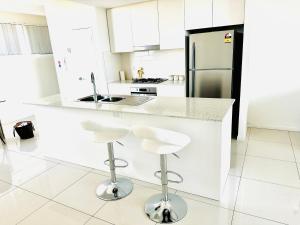 a white kitchen with a counter and stools at Modern 2 bedroom & 2 bathroom apartment with stunning Sydney CBD & Skyline Views! in Liverpool