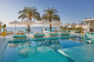 uma piscina com cadeiras e guarda-sóis e o oceano em Dorado Ibiza - Adults Only em Playa d'en Bossa