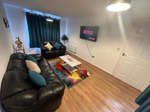 a living room with a leather couch and a tv at Trinity's Place in Wythenshawe