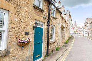 Minchinhampton的住宿－Maple Rose - 2 Bed with Garden in Minchinhampton!，一座砖砌的建筑,有一扇蓝色的门和一篮鲜花