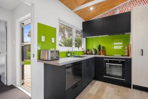 Changing Sands - Whiritoa Holiday Home في Whiritoa: مطبخ مع خزائن سوداء وجدران خضراء