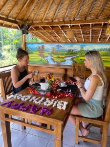 two women sitting at a wooden table with food at Kubu Penida Villa in Nusa Penida