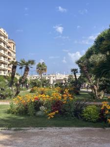a park with flowers and palm trees and a building at Queen Riviera : climatisation, parking, terrasse in Menton