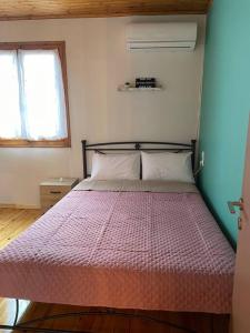 a bedroom with a bed with a pink comforter and two windows at Politis' wooden house in Vasiliki