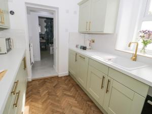 a kitchen with white cabinets and a wooden floor at Ty Arth in Llandudno +24 photos