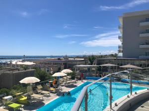 una piscina con ombrelloni e sedie e la spiaggia di Hotel Caesar a Lido di Savio