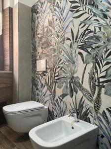 baño con aseo blanco y papel pintado de plantas en B&BUrszula Gizzeria Lido, en SantʼEufemia Lamezia