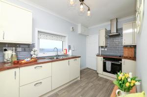 a kitchen with white cabinets and a sink and a window at Coleil Cottage in Garrabost