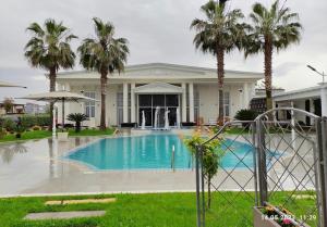 a swimming pool in front of a house with palm trees at Hotel Colis in Tirana