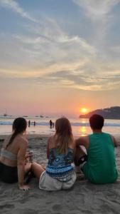 três pessoas sentadas na praia a ver o pôr-do-sol em Sohla Rooftop Hostel em San Juan del Sur