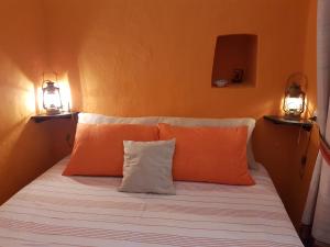 - un lit avec des oreillers orange et blanc et 2 lumières dans l'établissement dammusi, à Pantelleria