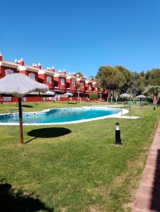 ein Pool mit einem Regenschirm im Gras in der Unterkunft Islantilla Club Golf in Huelva