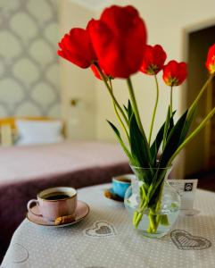 eine Vase mit roten Blumen und eine Tasse Kaffee auf dem Tisch in der Unterkunft Tamerlan in Chmelnyzkyj